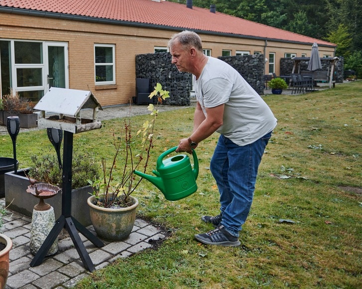 Beboer på døgntilbuddet Brommeparken vander blomster på terrasse